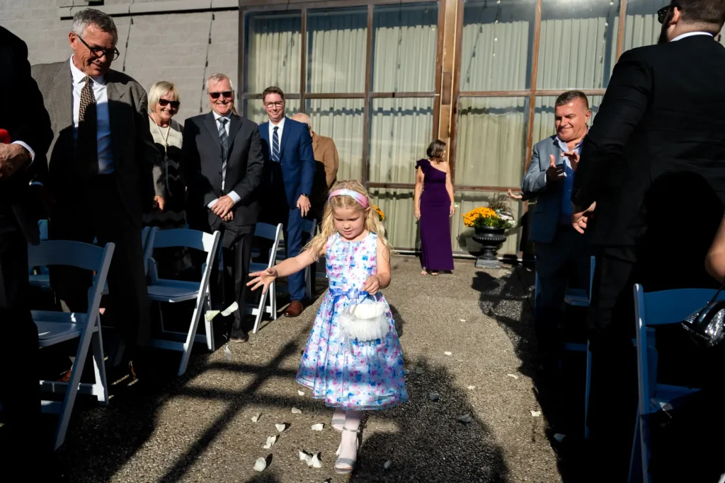 the flower girl spreads petals on the aisle as she walks down it. Shot at Carmen's event centre, Hamilton by Pixelesque Photography.
