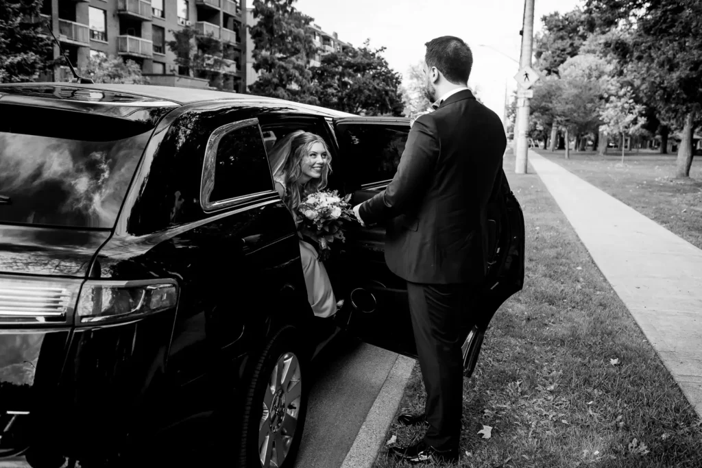 the groom holds the limo door open for his bride to exit. Shot at Hamilton's Gage Park by Pixelesque Photography.