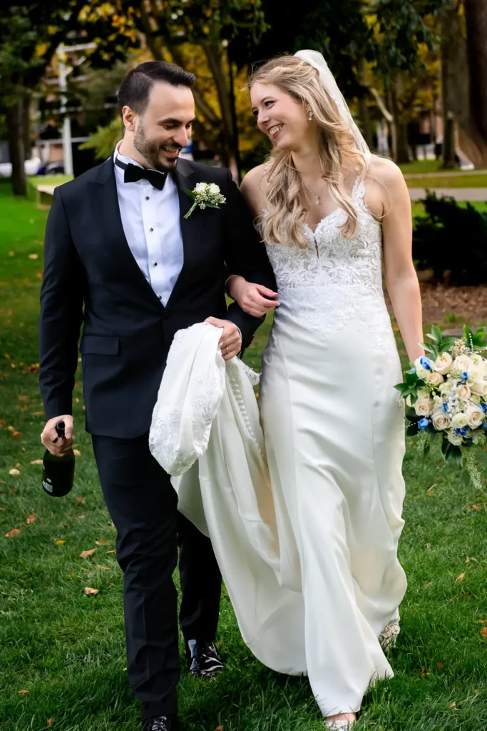 a wedding couple walk arm in arm as the groom holds a bottle of champagne. Shot at Hamilton's Gage Park by Pixelesque Photography.