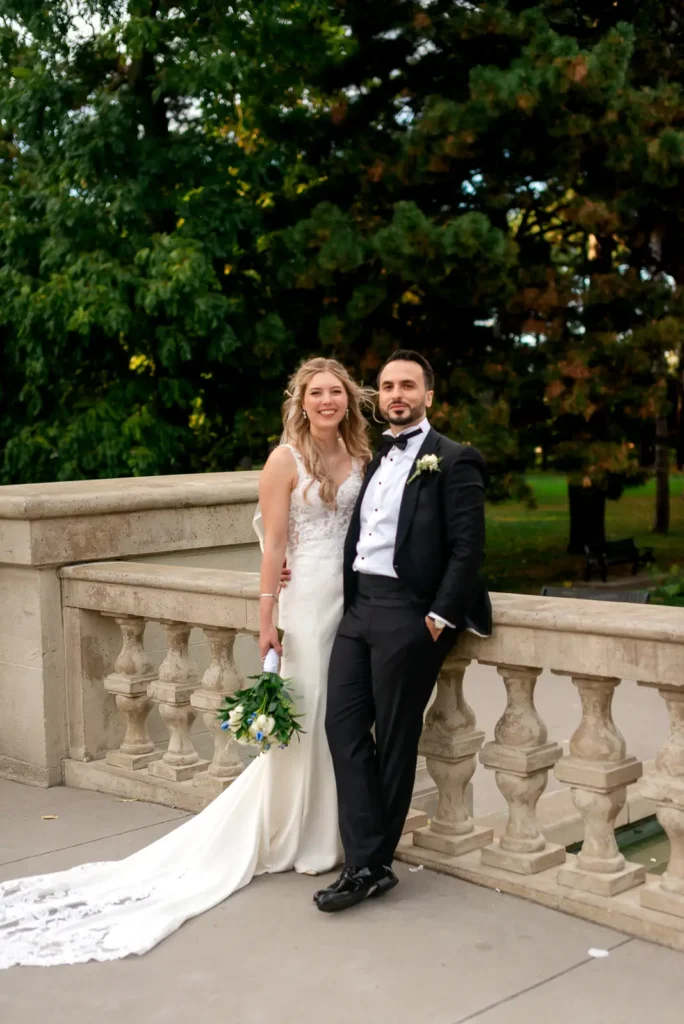 a wedding couple strikes a glamorous pose as they lean against a stone railing. Shot at Hamilton's Gage Park by Pixelesque Photography.