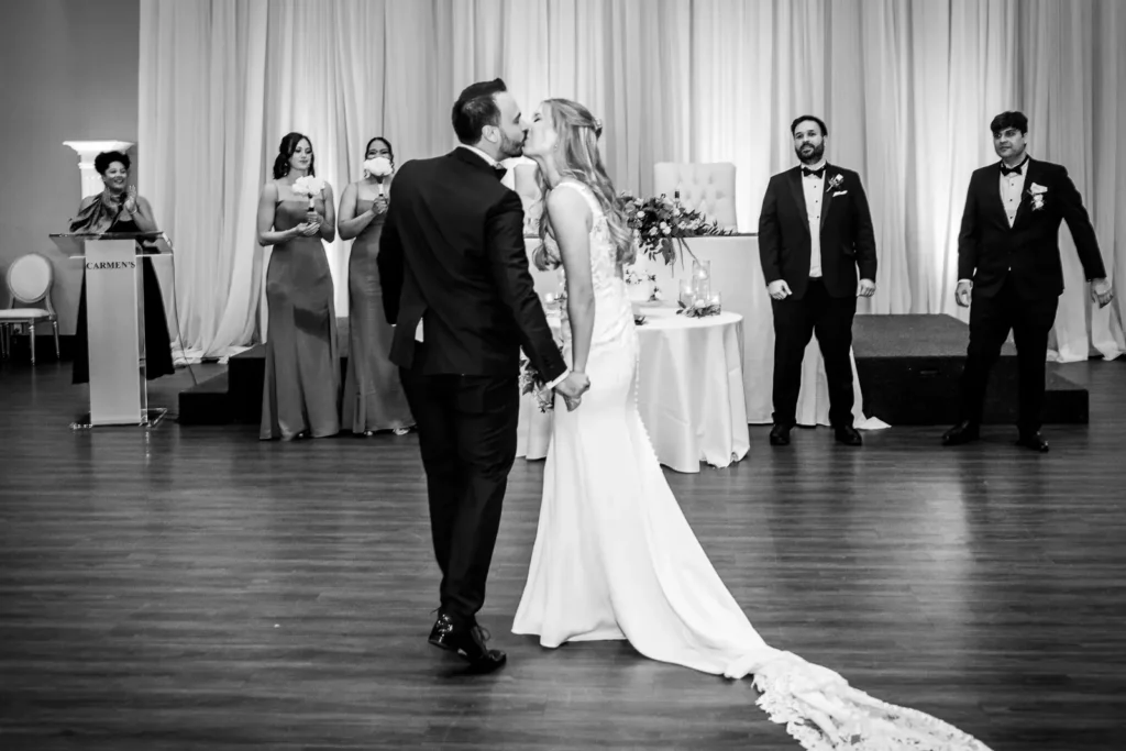 the wedding couple share a kiss after entering while heading to their seats. Shot at Carmen's Event Centre, Hamilton by Pixelesque Photography.