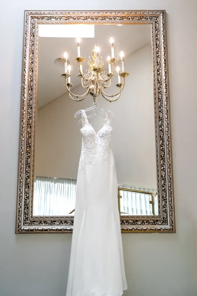 a wedding dress hangs off a light fixture on a large mirror. Shot at Carmen's event centre, Hamilton by Pixelesque Photography.