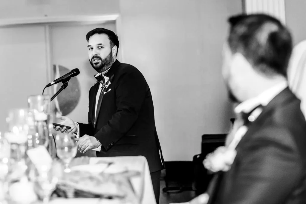 the best man looks at the groom from the podium as he gives his speech. Shot at Carmen's Event Centre, Hamilton by Pixelesque Photography.