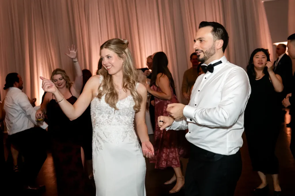 the bride and groom playfully point at someone on the dance floor. Shot at Carmen's Event Centre, Hamilton by Pixelesque Photography.
