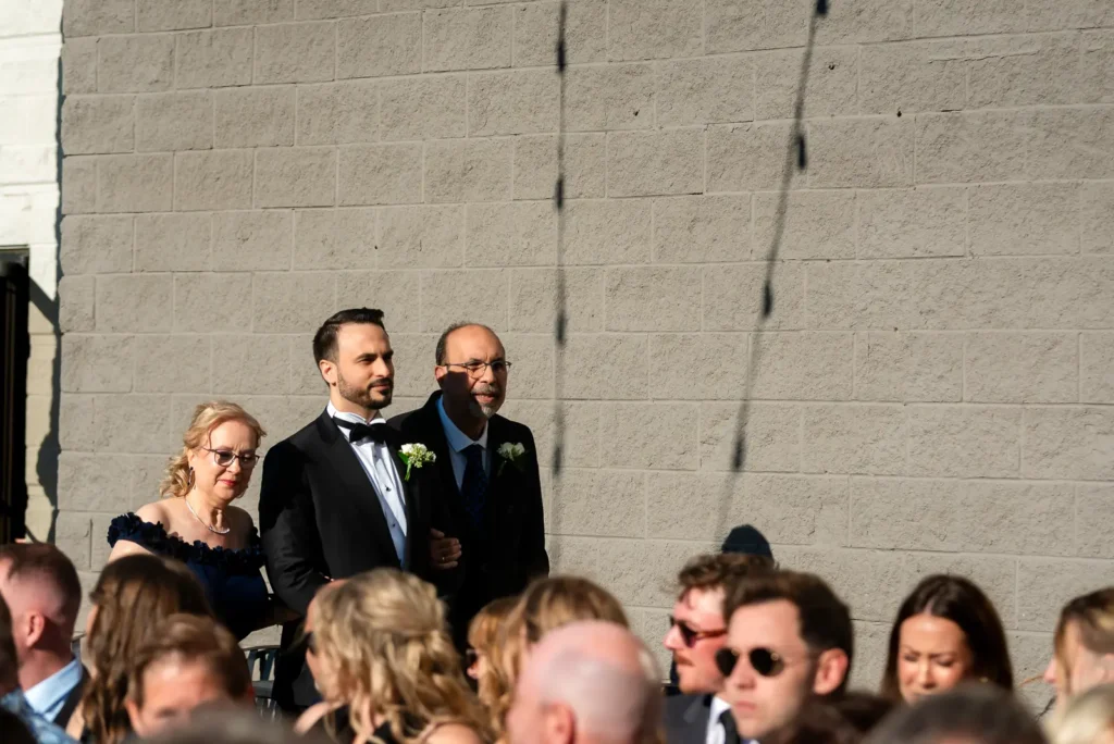 the groom enters the ceremony space in the sun with his parents. Shot at Carmen's event centre, Hamilton by Pixelesque Photography.