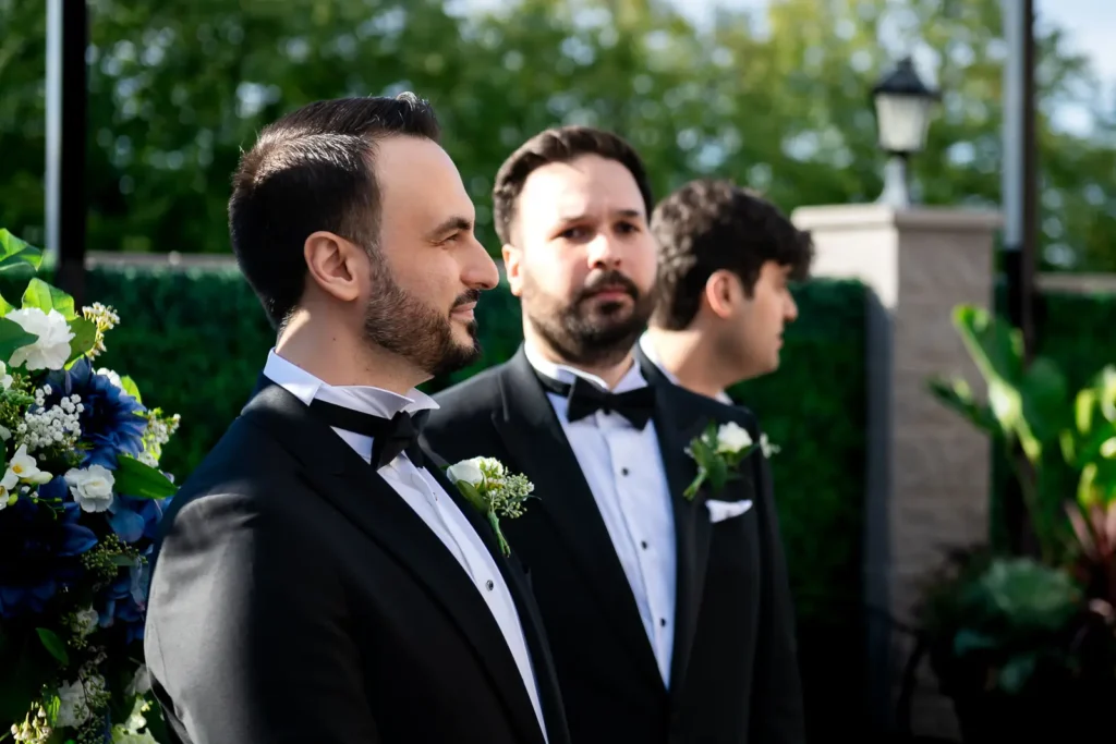the groomsmen look at the groom watching people walk down the aisle. Shot at Carmen's event centre, Hamilton by Pixelesque Photography.