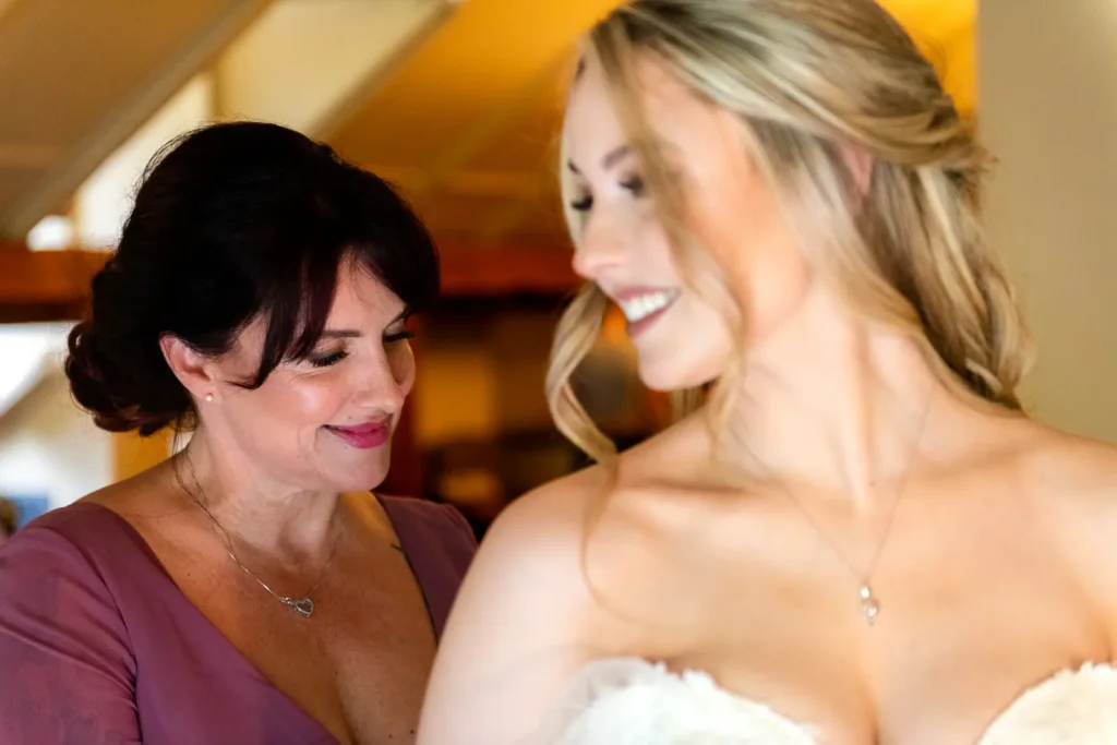 a mother zips up her daughter the bride's dress in the bridal suite at Ancaster Mill in Hamilton, Ontario.