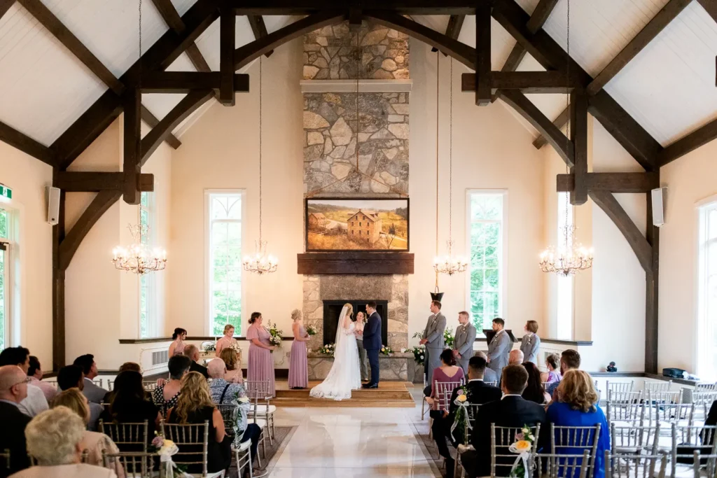 a wide view of the indoor chapel and the wedding couple and bridal party gathered at the altar at Ancaster Mill, Hamilton, Ontario.