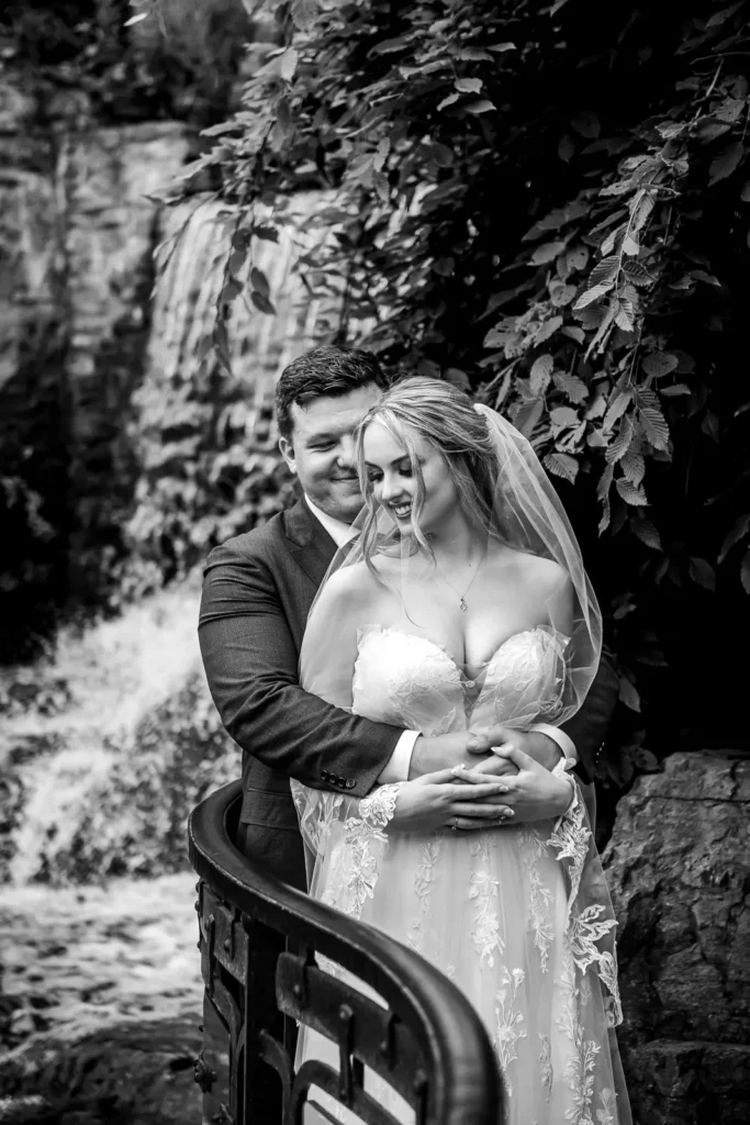 a groom holds his bride in front of the waterfall at Ancaster Mill in Hamilton, Ontario.