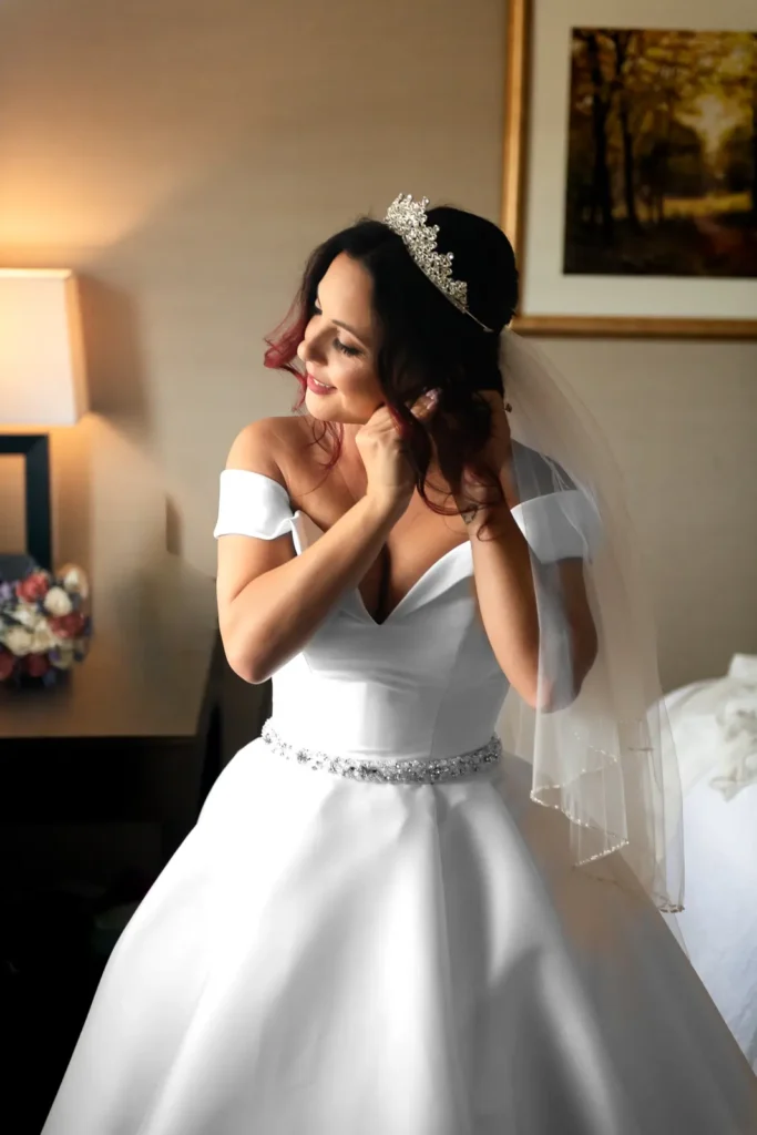 a bride fixes her earrings by a window.