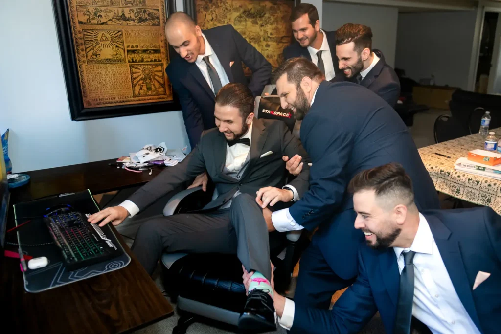 groomsmen pull a groom away from his computer as he holds on tight to it