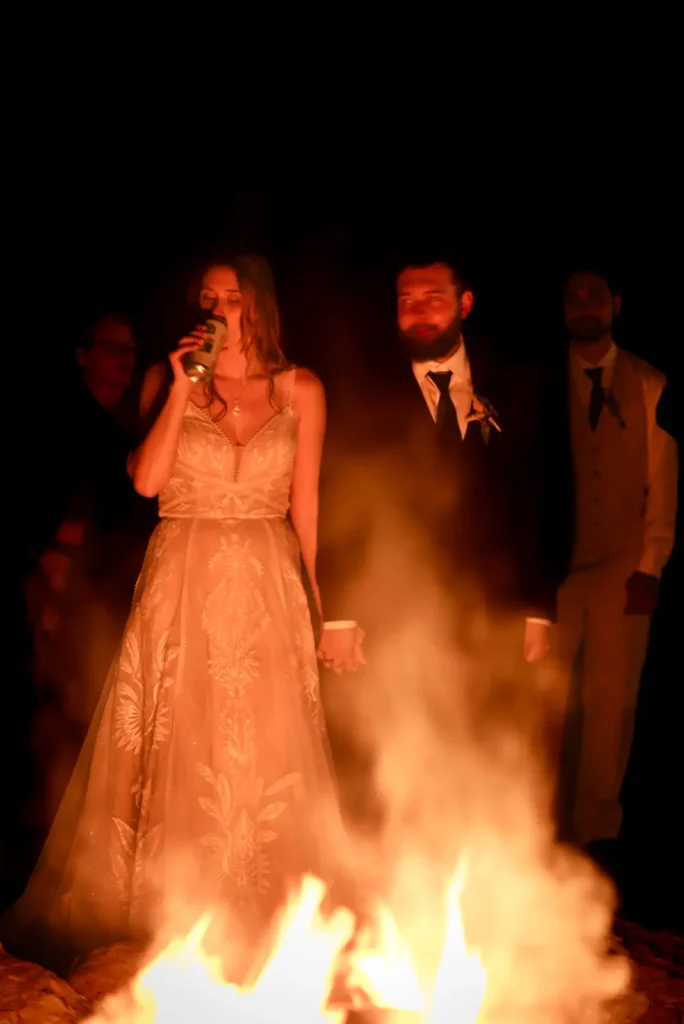 a bride and groom hold hands and watch a campfire roar at Homegrown Hideaway in Norfolk County, Ontario.