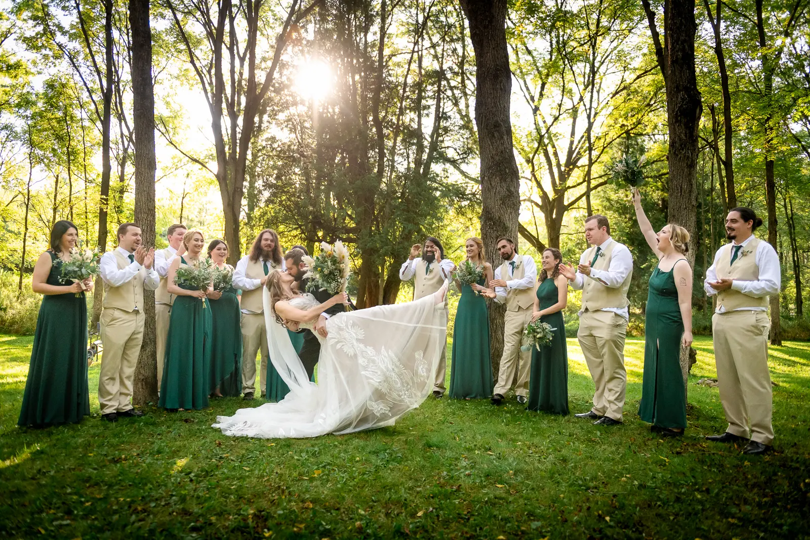 a groom dips and kisses his bride as the bridal party surrounds them in the woods at Homegrown Hideaway in Norfolk County, Ontario.