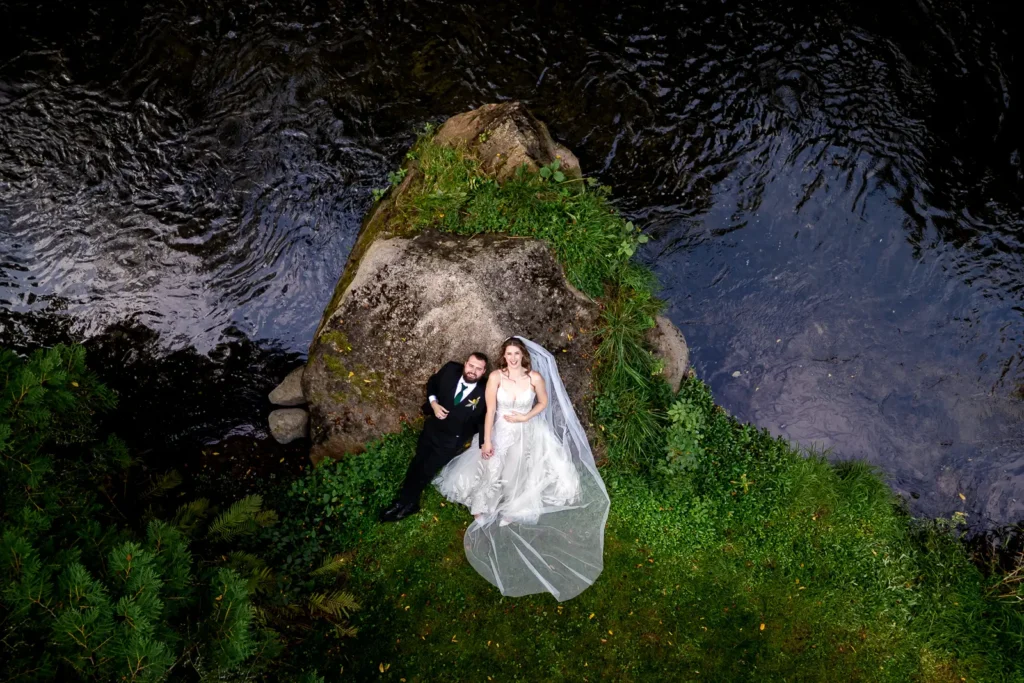 an overhead shot of a bride and groom laying on a rock as a river flows by them at Homegrown Hideaway in Norfolk County, Ontario.